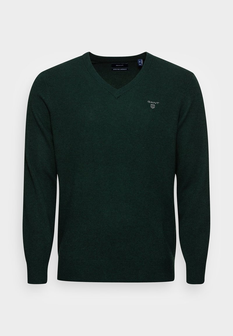 Pull vert en V en tissu tricot doux. Présente des manches longues et un petit logo sur la poitrine. Texture lisse et coupe ajustée.