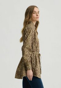 Bruine en beige leopardenprint blouse met lange mouwen, een ceintuur in de taille en een uitlopende design, gemaakt van gladde stof met een zachte textuur.
