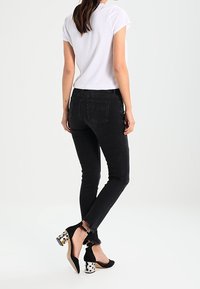 Czarne skinny jeans z postrzępionym dołem. Połączone z czarnymi szpilkami z kropkowanym i metalicznym obcasem. Modelka ubrana w białą koszulkę.