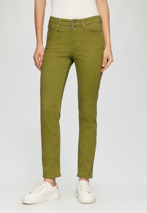 Jeans slim fit vert olive avec une taille mi-haute, cinq poches et des détails en métal argenté, associés à des baskets blanches.