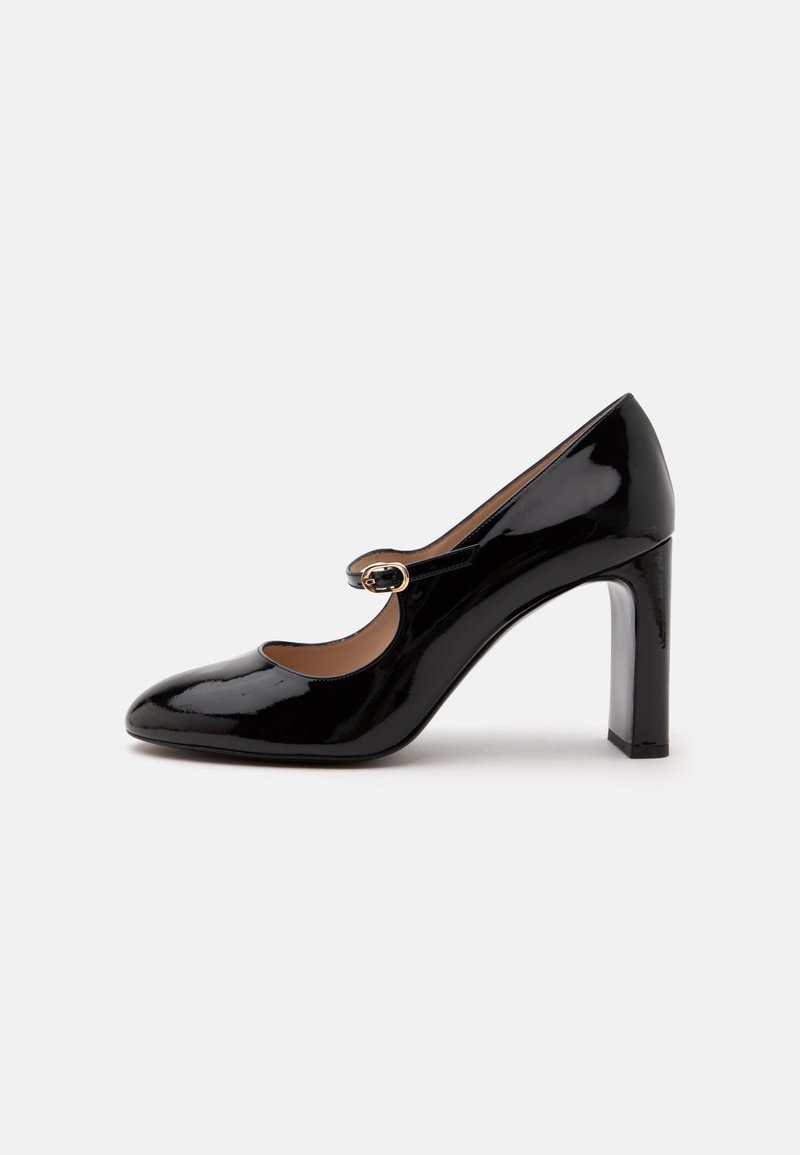 Chaussure Mary Jane à talon haut en cuir verni noir avec un bout arrondi et une petite sangle à boucle sur le coup de pied sur fond blanc.