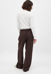 Braune weit geschnittene Hose mit einem elastischen Bund, kombiniert mit einem cremefarbenen Langarmoberteil. Das Outfit zeichnet sich durch ein schlichtes Design und eine weiche Textur aus.