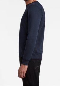 Marineblauer Pullover mit Rundhalsausschnitt, langen Ärmeln, gerippten Bündchen und Saum, aus weichem Baumwollmischgewebe. Seitenansicht gezeigt.