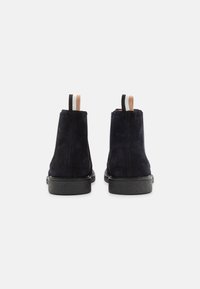 Bottines en suède bleu foncé avec une semelle en caoutchouc et des languettes contrastantes beige, noires et blanches à l'arrière.