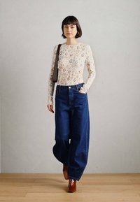 Μπλούζα με μακριά μανίκια και σχέδια με λουλούδια και ουράνια σώματα· τζιν παντελόνι με φαρδιά μπατζάκια και ψηλή μέση σε σκούρο χρώμα· καφέ μπότες με τακούνι· τσάντα ώμου.