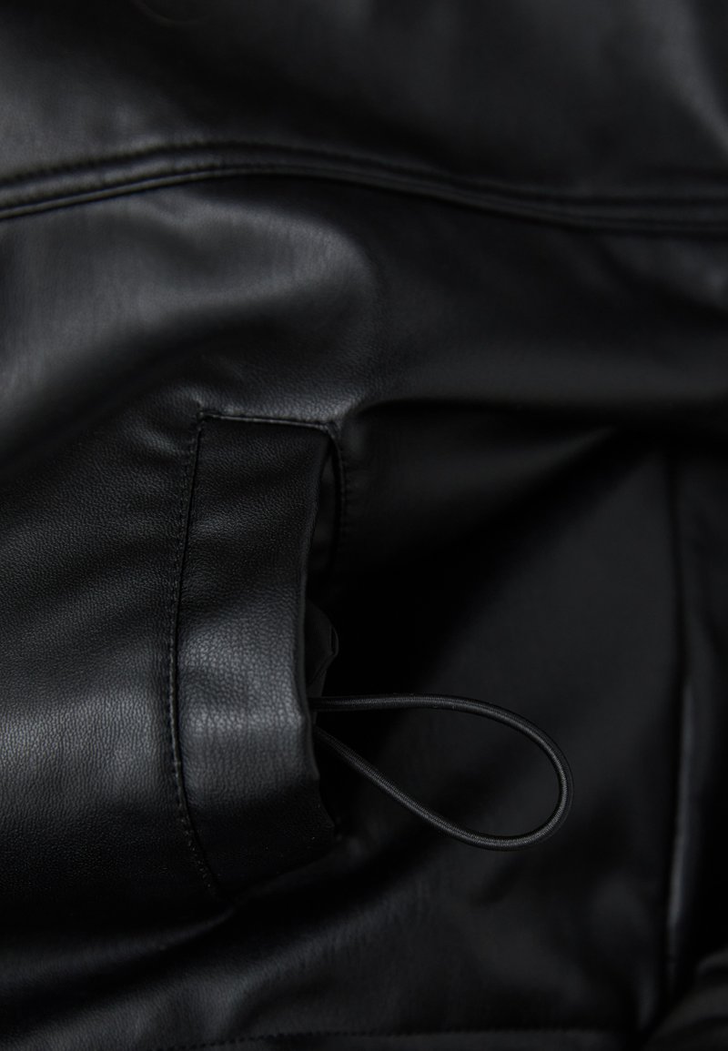 Interior de chaqueta de cuero negro con un acabado suave y texturizado. Incluye un pequeño bolsillo y un delgado cordón elástico para realizar ajustes.