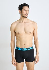 Schwarze Boxer-Briefs mit einem türkisfarbenen Puma-Logo am Bund. Hergestellt aus einem elastischen Stoff, bieten sie eine enganliegende Passform und kurze Beine.
