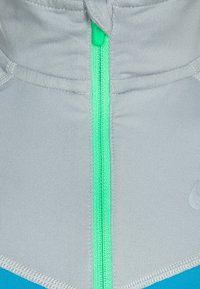 Šed�á bunda na zip s vysokým límcem, která má tyrkysové akcenty a texturední látku. Zip je zvýrazněn jasně zelenou barvou.