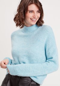 Pull en mohair bleu clair avec un col montant, des poignets côtelés et une texture douce. Associez-le à une jupe en cuir noire.