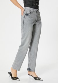 Jeans gris de tiro alto con un diseño de pierna recta, que presentan bolsillos delanteros y una textura desgastada. Llevados con zapatillas negras de puntera afilada.