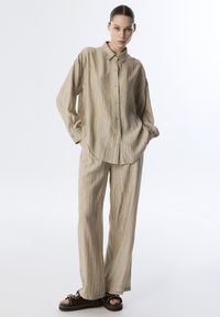 Beige, geweven overhemd met knopen en bijpassende wijde broek. Zachte stof met subtiele verticale strepen, gecombineerd met donkere plateausandalen.