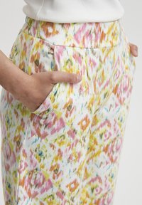 Spalvingos printuotos kelnės su daugiausia baltu fono, kuriame yra gyvų rožinių, geltonų ir akvatorijų dėmių. Turintis šonines kišenes.