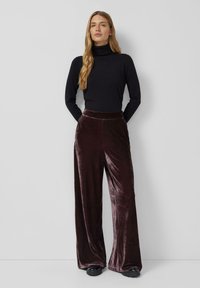 Zwarte coltrui en wijdvallende, donker bordeaux fluwelen broek. De soepele textuur, hoge taille en ontspannen pasvorm verhogen het comfort en de stijl.