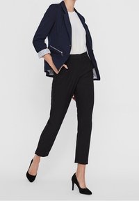 Marinblazer med silverfärgade dragkedjeaccenter, vit skjorta och svarta byxor. Stylad med svarta högklackade skor och rullad ärmdesign.