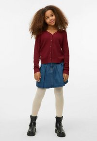 Tamsiai raudonas banguotas kardiganas su auksiniais širdelės mygtukais, derinamas su klostuota džinsine sijonu, smėlio spalvos pėdkelnėmis ir juodais kulkšninių batais.