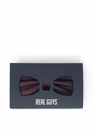 Dunkellila Fliege mit weißen Punkten, präsentiert in einer schwarzen Schachtel mit der Aufschrift "REAL GUYS" auf weißem Hintergrund.