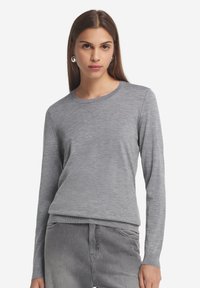 Grau langärmliger Pullover aus einem weichen, leichten Stoff mit rundem Ausschnitt und figurbetontem Schnitt, kombiniert mit grauen Jeans.