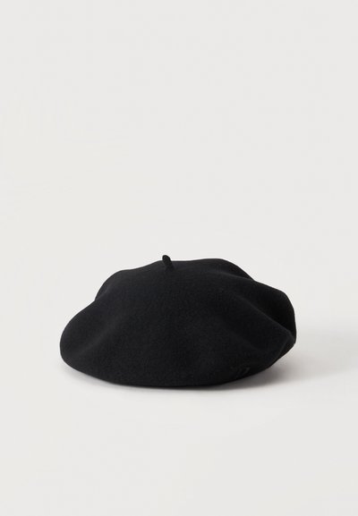 Béret en laine noire avec une petite boucle au sommet, reposant sur une surface blanche.