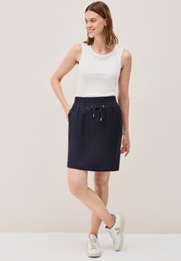 Marineblauwe rok met elastische taille en trekkoord, voorzien van zijzakken, gecombineerd met een wit mouwloos topje en witte sneakers.