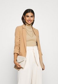 Beige blazer over a ribbed, light brown turtleneck, paired with cream wide-leg pants and holding a textured, light gray clutch.