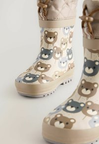 Bottes de pluie en caoutchouc avec un fond crème présentant un motif d'ours en brun, gris et bleu. Semelle texturée pour l'adhérence et haut ajustable.