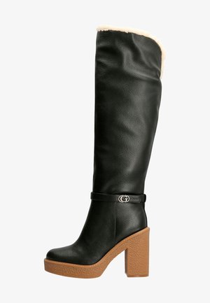 Zwarte leren kniehoogte laars met een zachte beige voering, een chunky bruine platformzool en een zilveren logo-accent op de enkelriem.