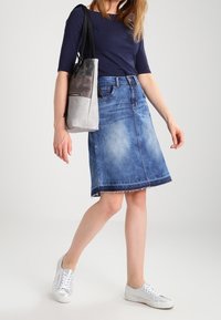 Falda de mezclilla en forma de A con un dobladillo deshilachado, combinada con una blusa oscura y un bolso gris. Zapatillas blancas completan el conjunto. Textura de tela suave.