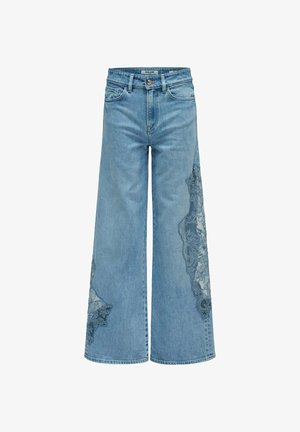 Jeans de pierna ancha color azul claro con parches de encaje en la pierna derecha y la parte inferior de la pierna izquierda, con bolsillos delanteros y cierre de botón.