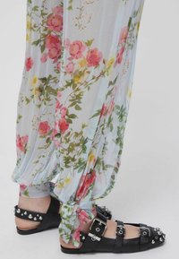 Pantalon ample à motif floral noué aux chevilles, accompagné de sandales plates noires avec boucles et clous argentés sur les orteils et les brides.