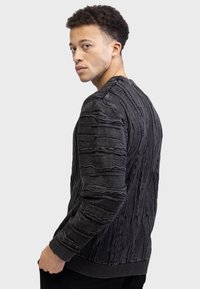 Black textured sweater featuring 3D wavy patterns, ribbed cuffs and hem, crew neckline, and a slim fit. Shown from a side angle.