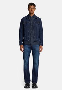 Giacca di jeans da uomo in blu scuro, caratterizzata da un taglio classico con due tasche frontali, chiusura a bottoni, dettagli cuciti e una camicia di jeans abbinata sotto.