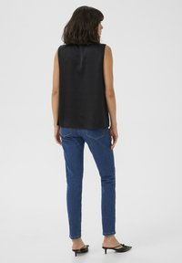 Czarna bezrękawnik o gładkiej fakturze, zestawiony z niebieskimi jeansami o slim fit. Całość dopełniają czarne klapki na wysokim obcasie.