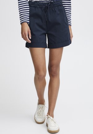 Shorts navy avec un ourlet roulé et une taille élastique. Associés à des baskets blanches, présentant une surface texturée et un design à lacets.