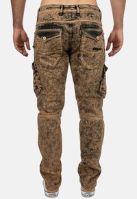 Pantaloni cargo marroni con una texture invecchiata, dotati di due tasche posteriori, tasche laterali e dettagli di cucitura a contrasto.