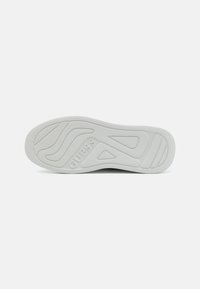 Semelle en caoutchouc blanc présentant des motifs texturés et le nom de la marque en relief "GUESS". Design global plat avec des sections contournées.