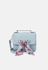 Vaaleansininen synteettinen nahkalaukku kultaisilla metalliosilla, yläkahvalla ja säädettävällä olkahihnalla. Edessä on sidottu kukkakuvioinen huivi.