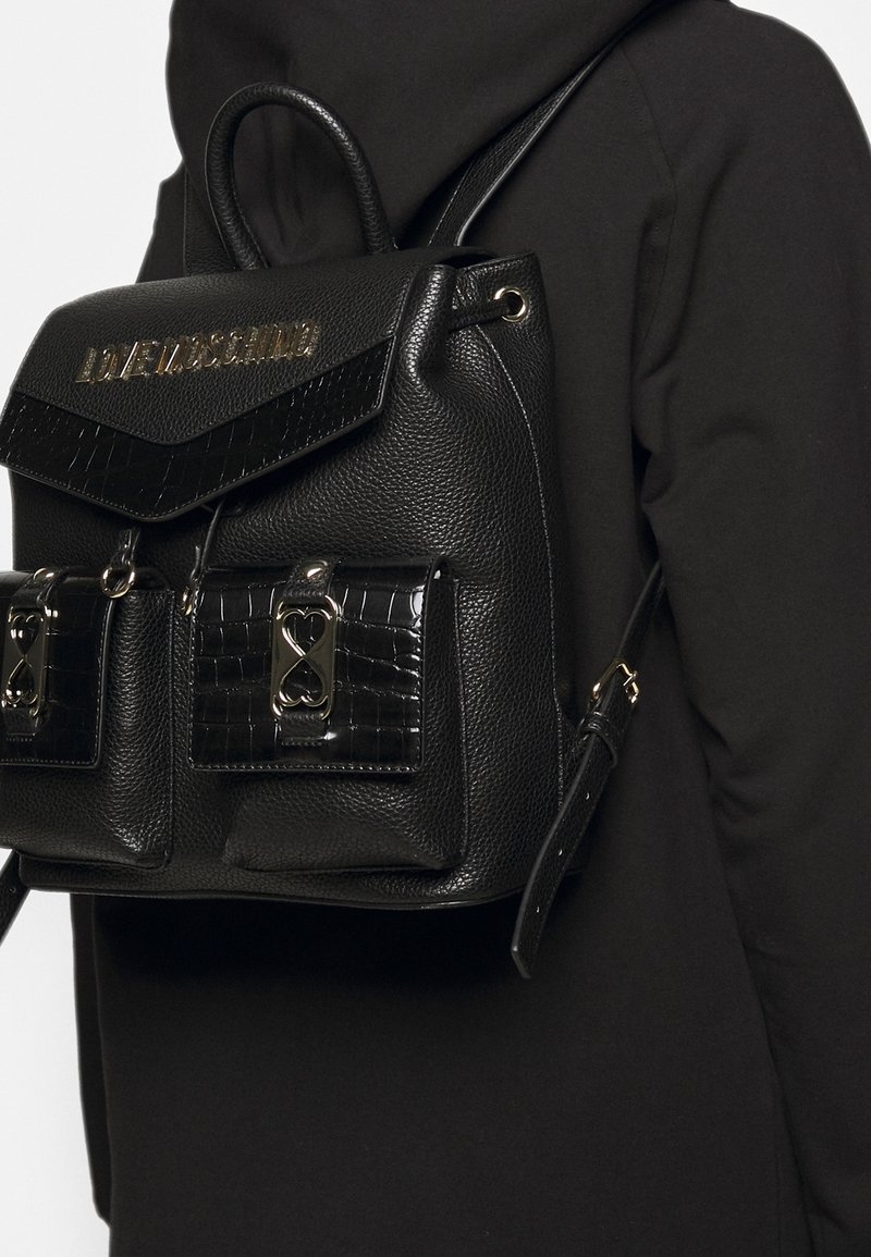 Svart läderryggsäck med texturerad yta, metalliska detaljer och två framfickor med krokodilpr Präglade detaljer.