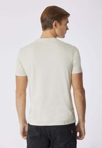 T-shirt beige a maniche corte realizzato in morbido cotone, con scollatura a girocollo e design semplice. Indossato con jeans scuri, visto da dietro.