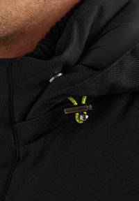 Schwarze Stoffjacke mit einem Reißverschlusskragen. Merkmale eine strukturierte Außenseite, glänzende Beschläge und einen neon-grünen Reißverschlussanhänger.