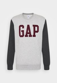 Šedá mikina s tmavě šedými rukávy, na přední straně s velkým maroon logem „GAP“. Vyrobeno z měkké, strukturální látky.