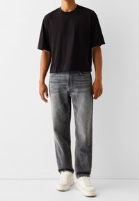 Svart t-shirt med kort ärm kombinerat med urtvättade grå jeans som har subtila slitningar. Bärs med kraftiga vita sneakers.