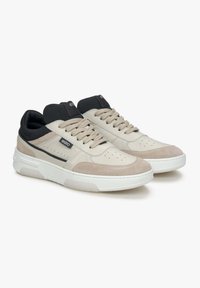 Beige en grijze sneakers met een mix van leer en suede materialen, met een geperforeerde neus en een witte rubberen zool. Zwarte accenten op de hiel.
