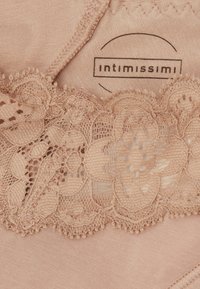 Lingerie en dentelle beige avec des motifs floraux complexes. Tissu doux au toucher lisse, portant une étiquette avec la mention "Intimissimi."