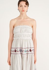 Strapless jurk met witte strepen, met een gathering bij het lijfje en een gelaagde rok. Kenmerkt kleurrijke bloemenborduursels langs de zoom. Katoenen stof.
