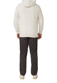 Jasnobeżowa bluza z kapturem w zestawieniu z ciemnoszarymi spodniami. Strój charakteryzuje się luźnym krojem i prostym wzornictwem, dopełnionym białymi butami.