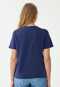 Marineblauw T-shirt met korte mouwen, ronde hals en een gladde textuur, gedragen met lichtblauwe denim jeans. Eenvoudig en onopgesmukt ontwerp.