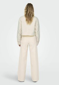 Veste crème raccourcie avec des manches perforées associée à un pantalon large crème. Texture lisse avec des coutures minimales et des poches.