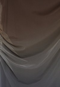 Gros plan sur un tissu en maille brun et gris superposé, transparent, avec une texture fine de résille visible et des plis doux créant des ombres subtiles.
