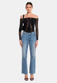 Schwarzer Netz-Body mit schulterfreiem Design, durchsichtigen Einsätzen, kombiniert mit hellblauen geraden Jeans, Absätzen und einer kleinen schwarzen Tasche.