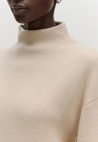 Beige coltrui gemaakt van zacht breimateriaal, met een minimalistisch ontwerp, een gladde textuur en subtiele naden.